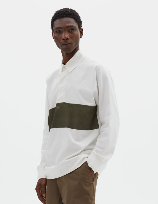 Cropped body image, front view of model wearing off white rugby long sleeve polo shirt with dark green panel across chest, twill collar, wide fly front placket and rib cuffs. Styled with green trousers.