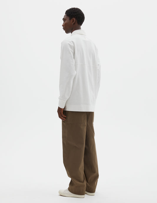 Full body image, back view of model wearing off white rugby long sleeve polo shirt with twill collar and rib cuffs. Styled with green trousers and beige canvas trainers.