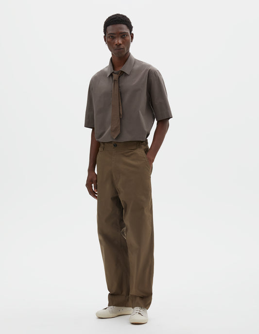 Full body image, front view of model wearing brownish green trousers with tapered leg, button fastening, side elasticated waistband, wide belt loops and deep hem. Styled with green shirt, green tie and beige trainers.