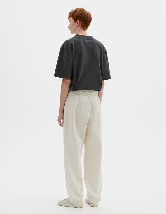 Full body image, back view of model wearing relaxed white joggers with elasticated waist and patch back pocket. Styled with greenish blue t-shirt and beige canvas trainers.