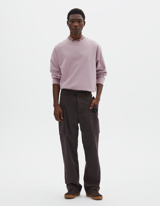Full body image, front view of model wearing dark brown cotton drill cargo trousers with hand in deep flap button fastening patch pocket, concealed hand pockets and belt loops. Styled with pink long sleeve t-shirt with sleeves rolled up over dark pink shirt, tucked in, and dark brown nubuck trainers.