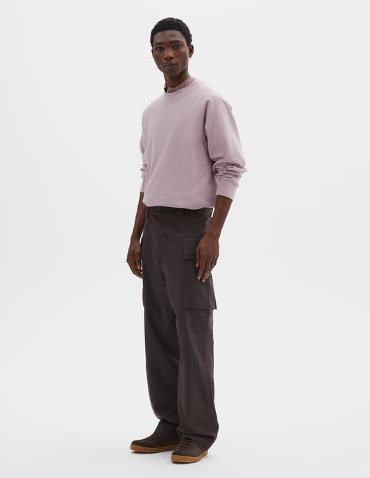 Full body image, side view of model wearing dark brown cotton drill cargo trousers with deep flap button fastening patch pocket, concealed hand pockets and belt loops. Styled with pink long sleeve t-shirt with sleeves rolled up over dark pink shirt, tucked in, and dark brown nubuck trainers.