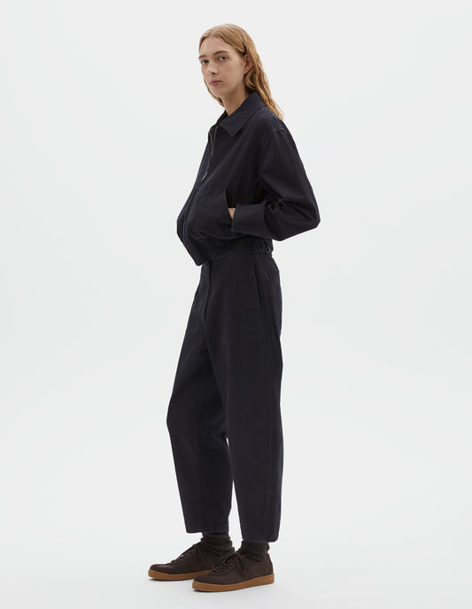 Full body image, front view of model wearing cropped boxy dark blue jacket with zip fastening, deep slanted welt pockets with reinforced stitch detailing and rib elasticated waistband. Styled with matching trousers and dark brown socks with dark brown nubuck trainers.