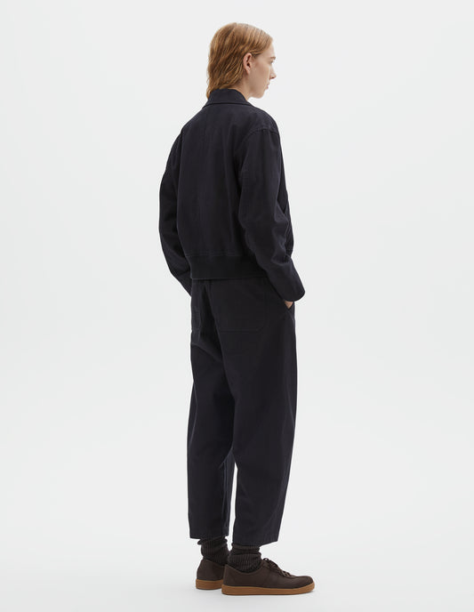 Full body image, back view of model wearing cropped boxy dark blue jacket with rib elasticated waistband. Styled with matching trousers and dark brown socks with dark brown nubuck trainers.