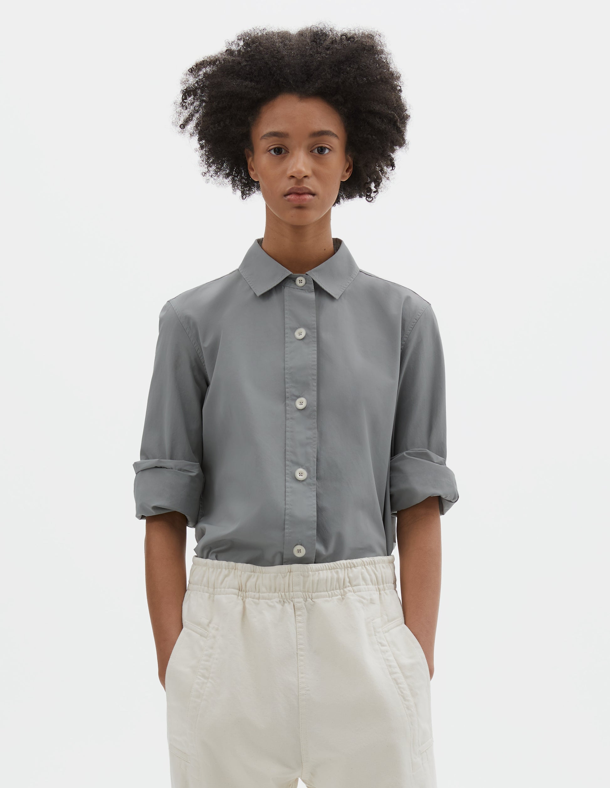 Cropped body image, front view of model wearing grey regular cut shirt with stitch through raised placket with corozo buttons on placket and cuffs. Styled with beige joggers.