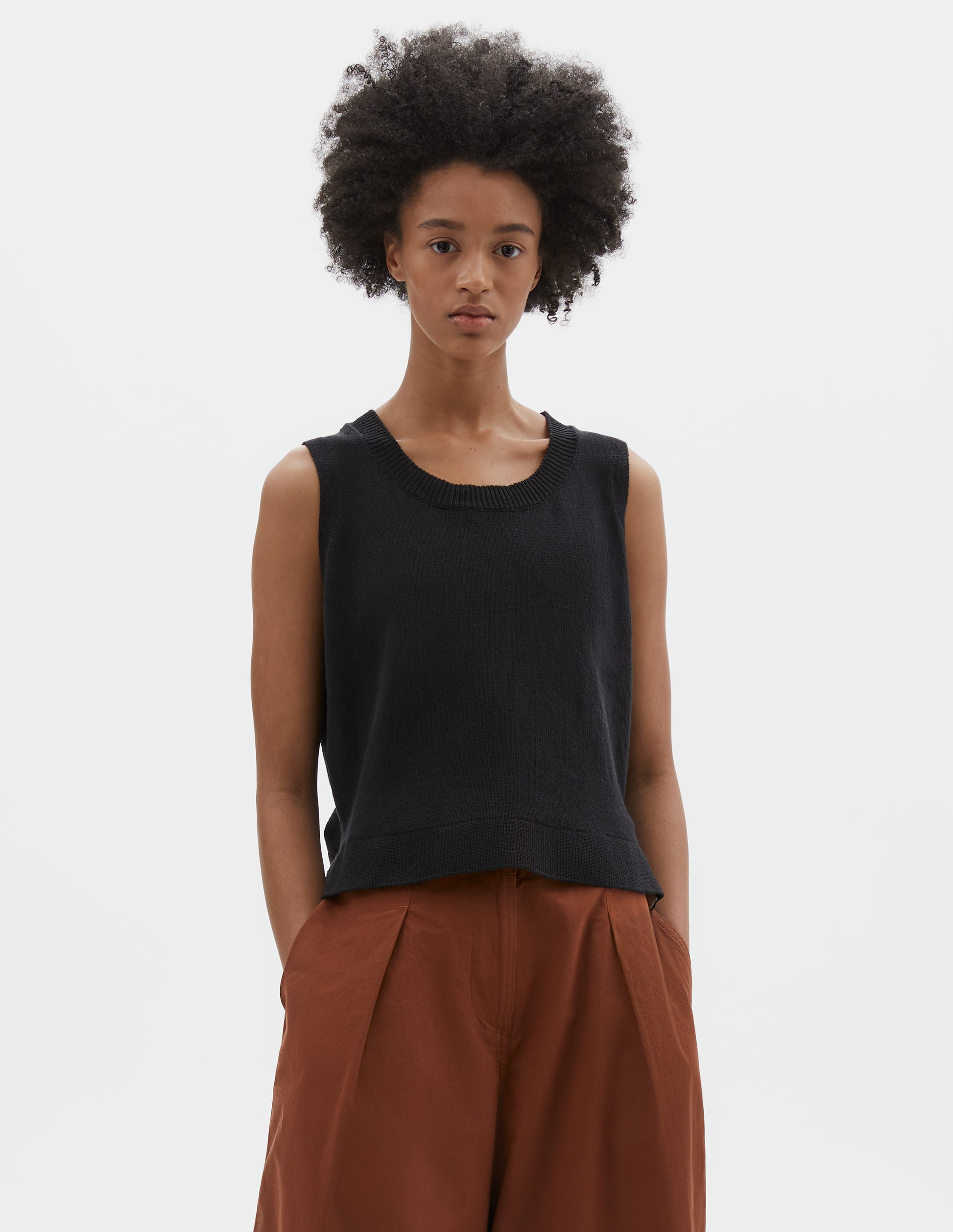 Cropped body image, front view of model wearing regular fit black knitted tank top with single rib crew neck and side split rib hem. Styled with dark orange culottes