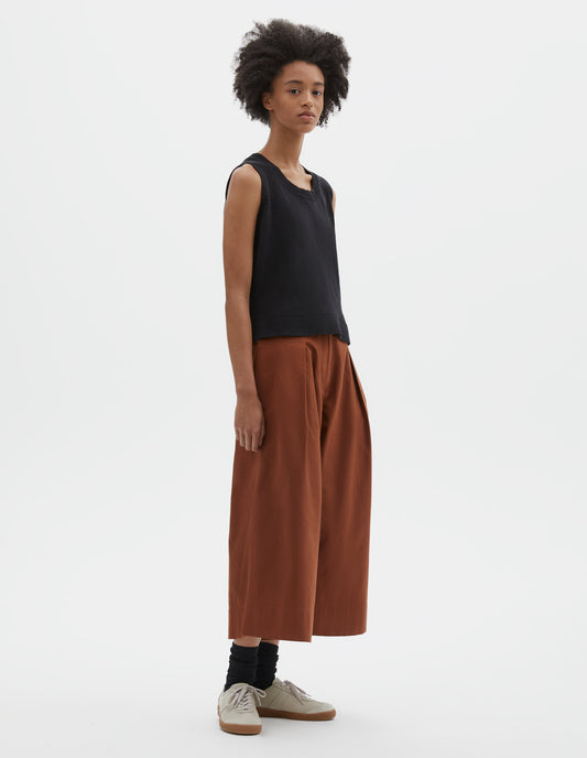 Full body image, front view of model wearing regular fit black knitted tank top with single rib crew neck and side split rib hem. Styled with dark orange culottes and black socks with beige nubuck trainers.