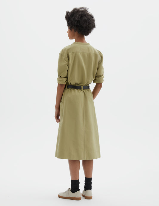 Full body image, back view of model wearing relaxed light green skirt with side pockets, elasticated waist and belt loops. Styled with pale green shirt, black leather belt, black socks and beige nubuck trainers.
