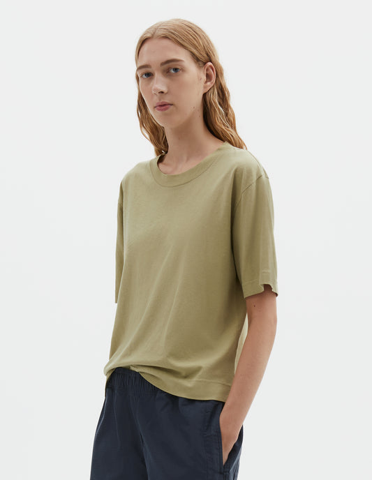 Cropped body image, front view of model wearing pale green cotton linen short sleeve t-shirt with vent split hem. Styled with dark navy wide leg trouser.