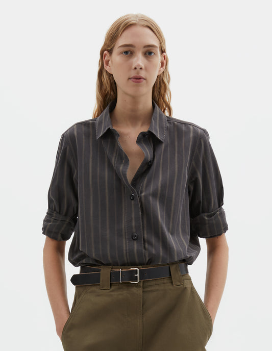 Cropped body image, front view of model wearing off black and khaki striped shirt, with corozo button fastening. Styled tucked in to green cotton skirt, with black leather belt. 