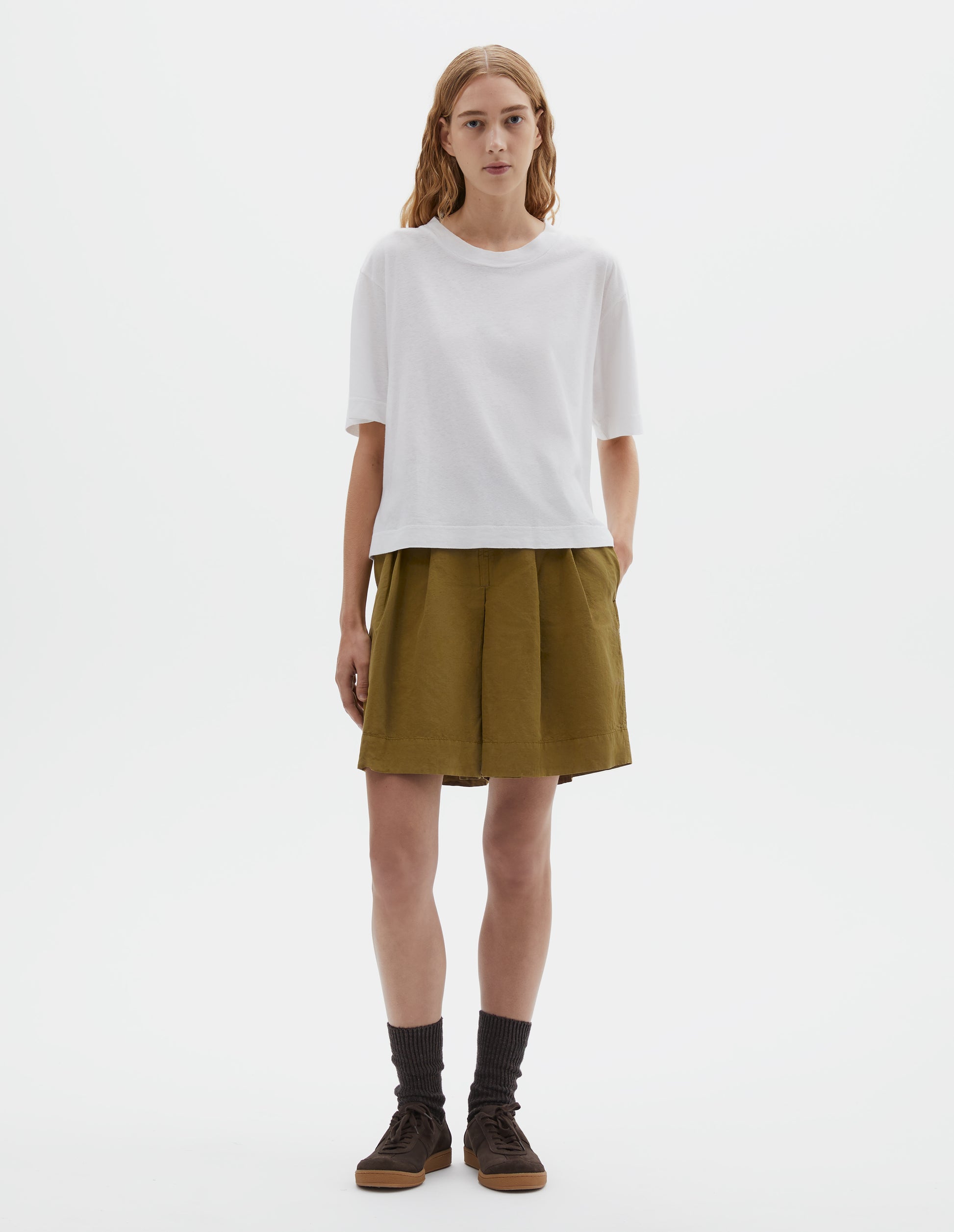 Full body image, front view of model wearing white short sleeve cotton t-shirt with contrast rib on neck. Styled with olive green shorts, grey socks and brown suede trainers.