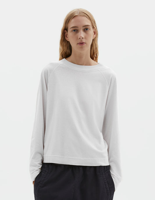Cropped body image, front view of model wearing white cotton linen long sleeve t-shirt with contrast rib on neckline and raglan sleeve detailing. Styled with dark navy joggers.