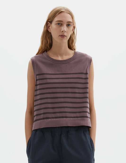 Cropped body image, front view of model wearing purple cotton linen tank top with brown stripes, contrast ribbing on neckline and armholes, with side split hem and deep stitch hem. Styled with dark blue trousers.