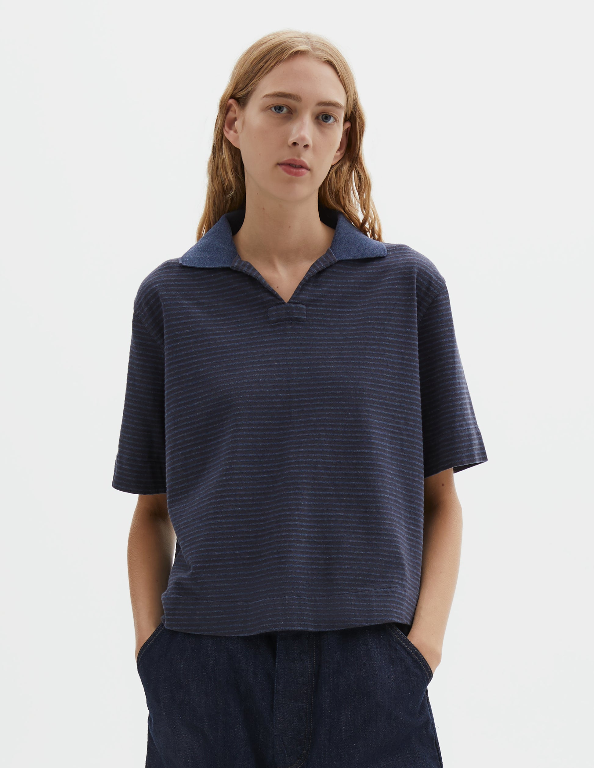 Cropped body image, front view of model wearing dark blue and light blue striped polo t-shirt, with open neck contrast melange rib collar and side split hem. Styled with indigo blue denim shorts. 