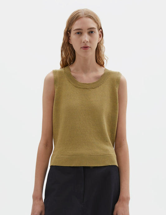 Cropped body image, front view of model wearing regular fit yellowish green knitted tank top with single rib crew neck and side split rib hem. Styled with dark blue trousers.