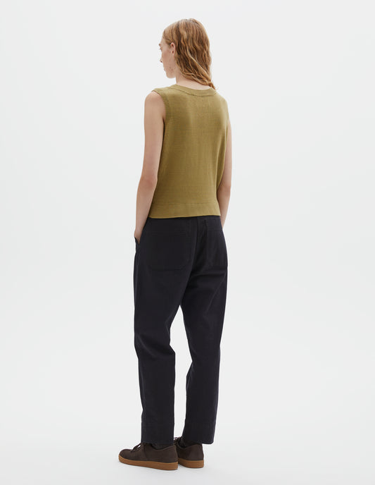 Full body image, back view of model wearing regular fit yellowish green knitted tank top with single rib crew neck and side split rib hem. Styled with dark blue trousers and dark brown nubuck trainers.