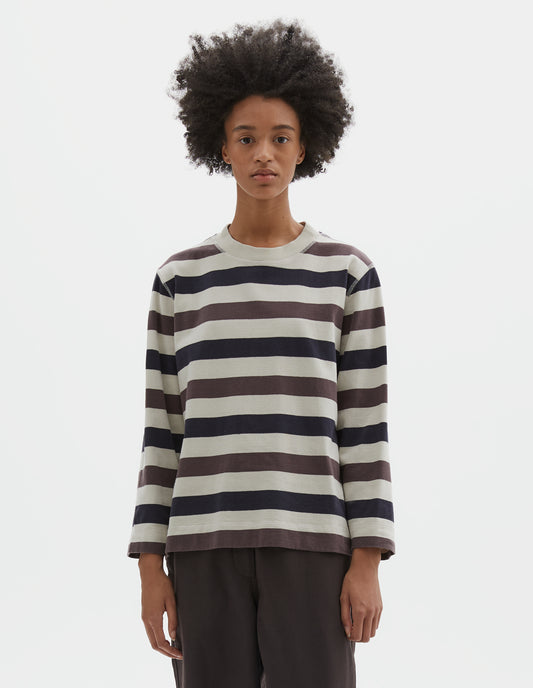 Cropped body image, front view of model wearing off white, dark navy and purple striped long sleeve top, with contrast rib on neckline and flatlock stitch detailing. Styled with brown trousers.