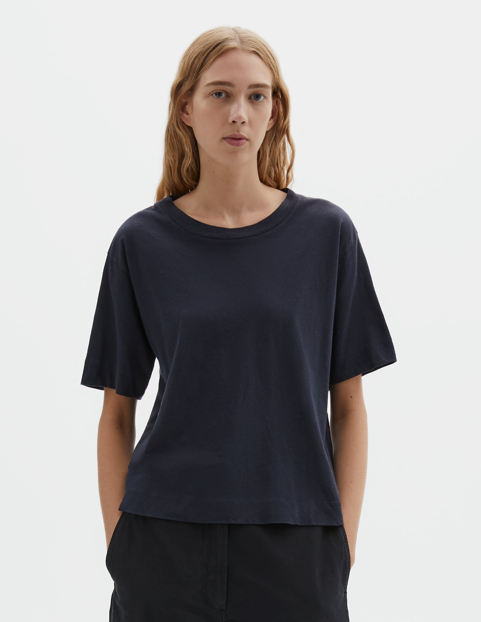 Cropped body image, front view of model wearing navy blue short sleeve cotton t-shirt with contrast rib on neck. Styled with indigo blue trousers.