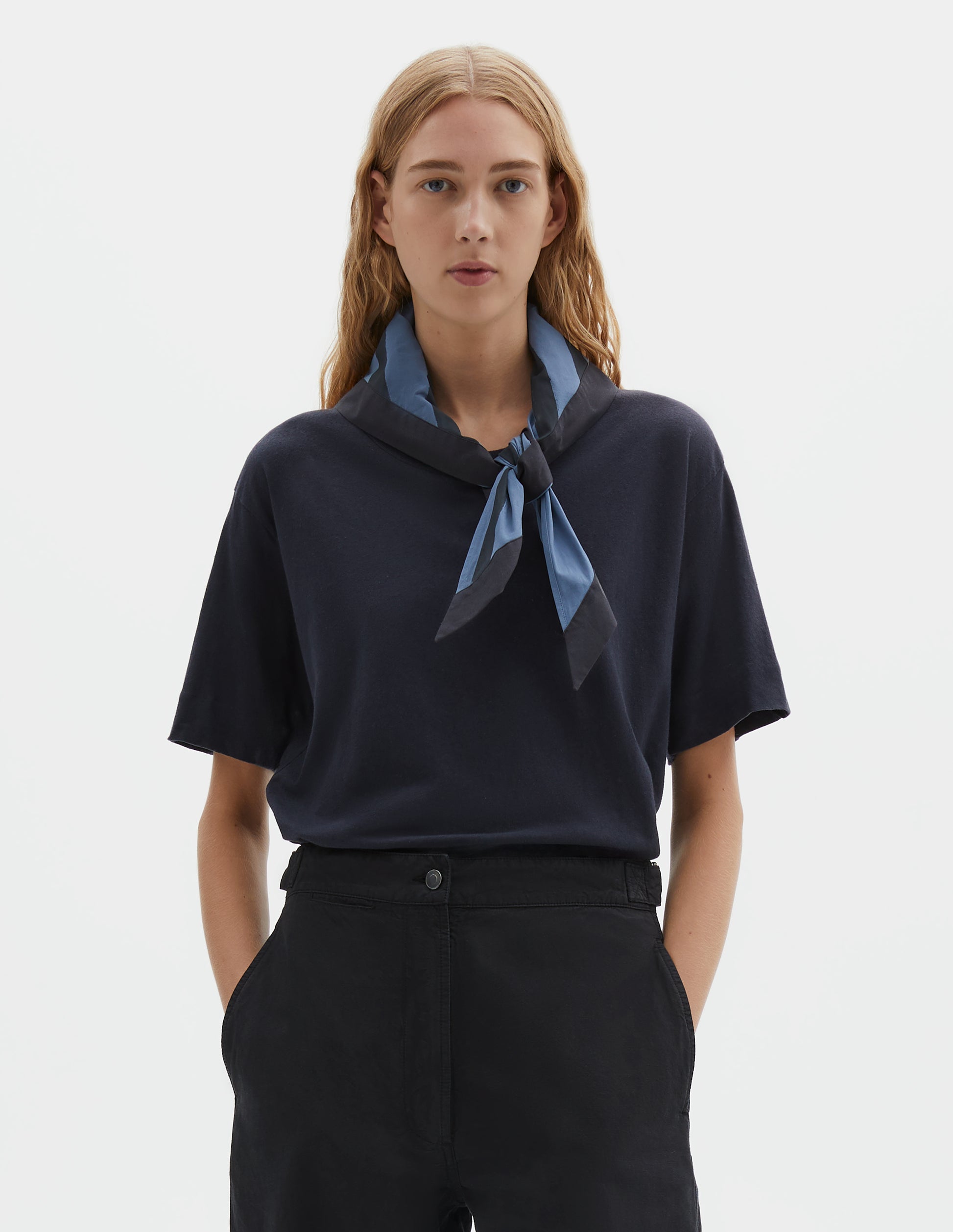 Cropped body image, front view of model wearing a Greyish blue and dark blue striped cotton scout scarf. Styled with a dark blue t-shirt and dark blue trousers.
