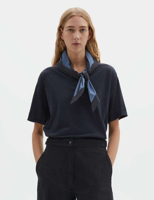 Cropped body image, front view of model wearing a Greyish blue and dark blue striped cotton scout scarf. Styled with a dark blue t-shirt and dark blue trousers.