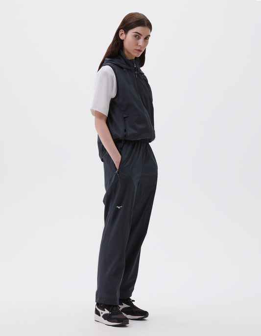 Full body image, front view of model wearing dark blue regular cut gilet with zip side pockets, zip fastening, hood with elastic adjuster and small white Mizuno logo, styled with white t-shirt and dark blue trousers with black, brown and white trainers.