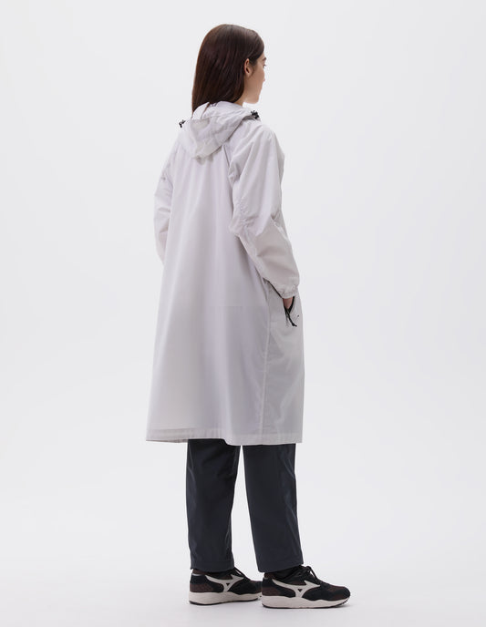 Full body image, back view of model wearing light grey boxy relaxed cut hooded coat, zip side pockets and elasticated cuffs, styled with dark blue trousers and black, brown and white trainers.
