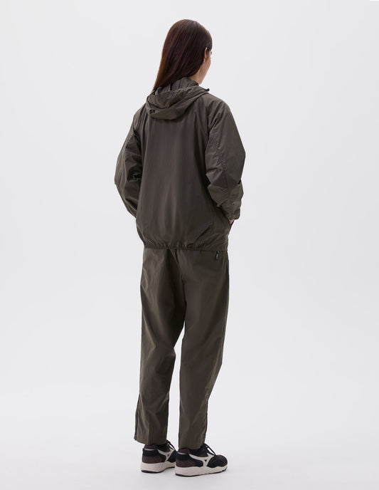 Full body image, back view of model wearing green regular cut jacket with hood and elasticated hem, styled with green trousers and black, brown and white trainers.