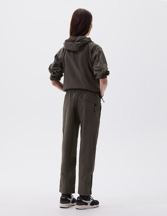 Full body image, back view of model wearing dark green relaxed cut trousers with zip welt back pocket and zip on hem, styled with matching jacket with hood and black, brown and white trainers.