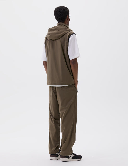 Full body image, back view of model wearing green/brown sleeveless gilet with adjustable hood and concealed zip side pockets. Styled with white t-shirt, matching green/brown trousers and black and brown trainers.