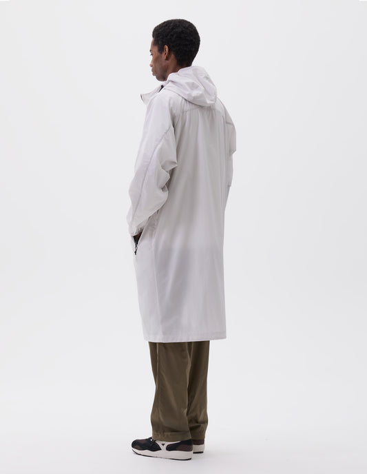 Full body image, back view of model wearing light grey rain parka with peaked elasticated hood and contrast zip fastening pockets. Styled with green trousers and black and brown trainers.