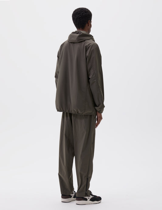 Full body image, back view of model wearing green/brown lightweight rain jacket with adjustable hood and elasticated hem. Styled with matching green/brown trousers and brown and black trainers.