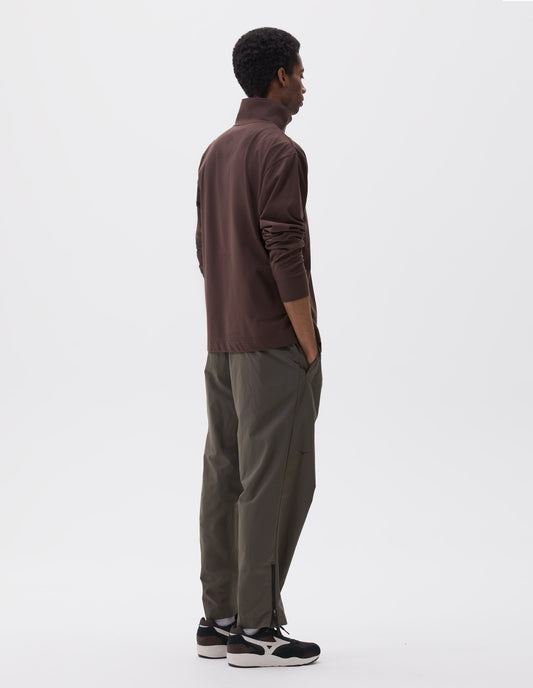 Full body image, back view of model wearing brown relaxed cut high neck half zip sweatshirt, styled with green trousers and black and brown trainers.