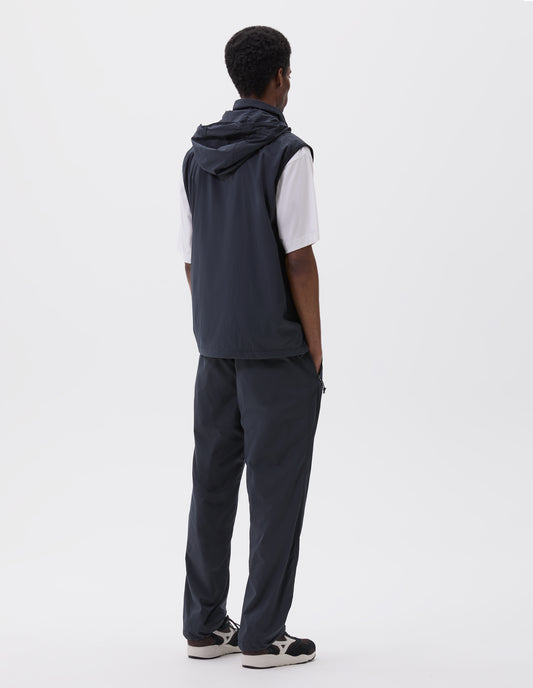 Full body image, back view of model wearing dark navy sleeveless gilet with adjustable hood and concealed zip side pockets. Styled with white t-shirt, matching dark navy trousers and black and brown trainers.
