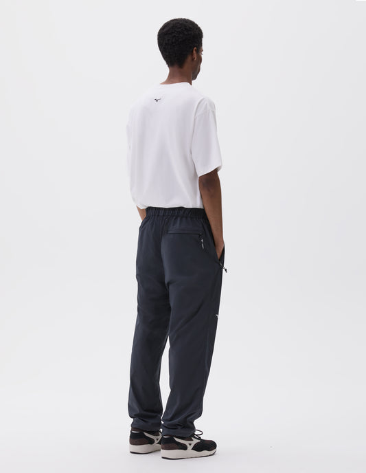 Full body image, back view of model wearing dark navy trousers with elasticated waist with toggle cinch adjuster, elasticated hems and zipper back pocket. Styled with white t-shirt with and brown and black trainers.