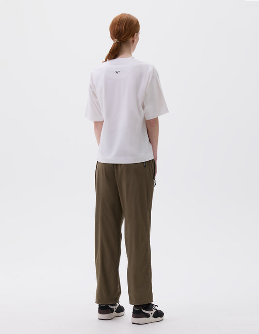 Full body image, back view of model wearing white relaxed t-shirt with small black Mizuno logo, styled with green trousers with zip side pockets and black, brown and white trainers.