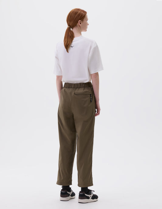Full body image, back view of model wearing relaxed green trousers with zip welt back pocket and elasticated waist, styled with white and black t-shirt and black, brown and white trainers.
