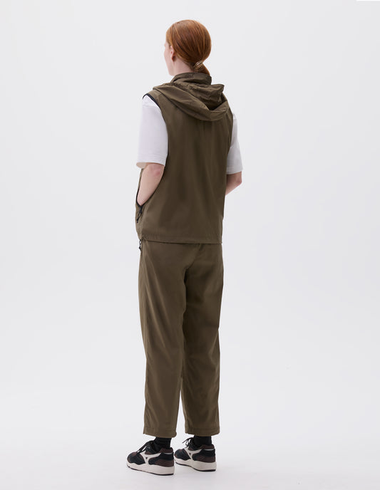 Full body image, back view of model wearing green regular cut gilet with hood, styled with white t-shirt and green trousers and black socks with black, brown and white trainers.