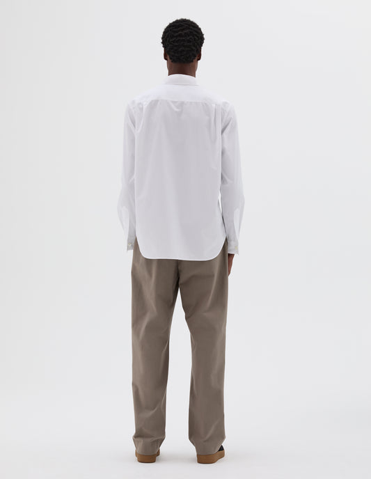 Full body image, back view of model wearing single pleated grey/beige trousers. Styled with white cotton shirt and black nubuck trainers.