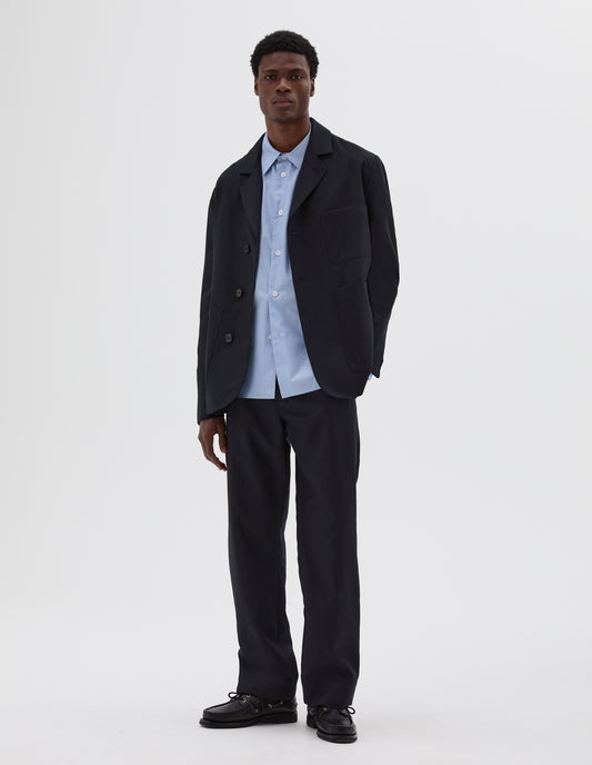 Full body image, front view of model wearing dark navy blazer with horn button closure and chest pocket. Styled with blue shirt, matching dark navy trousers and black leather boat shoes.