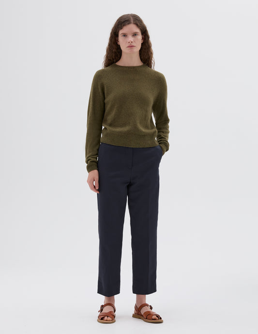Full body image, front view of model wearing green relaxed crew neck jumper with raglan sleeves, styled with dark blue cropped trousers and light brown leather sandals.
