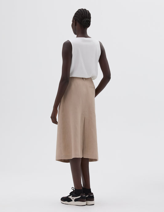 Full body image, back view of model wearing beige midi length back vent skirt with back pocket, belt loops, styled with a white vest, black socks and black and brown trainers.