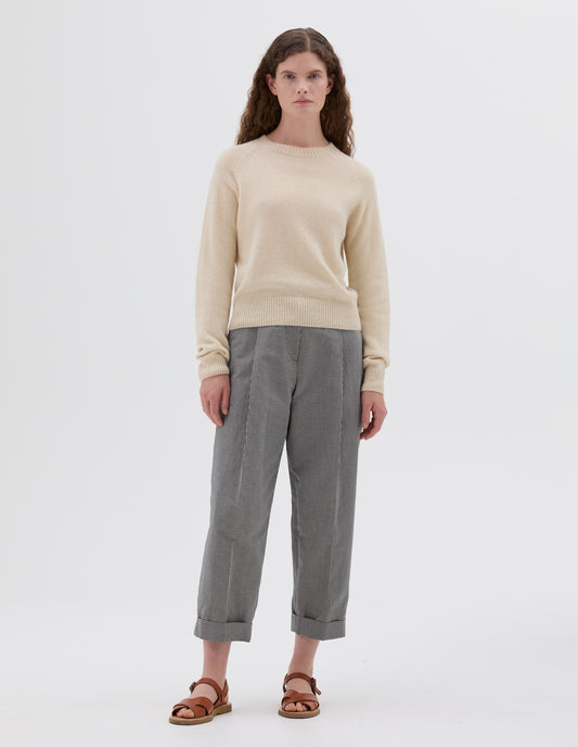 Full body image, front view of model wearing beige relaxed crew neck jumper with raglan sleeves, styled with black and white gingham pleated trousers with light brown leather sandals.