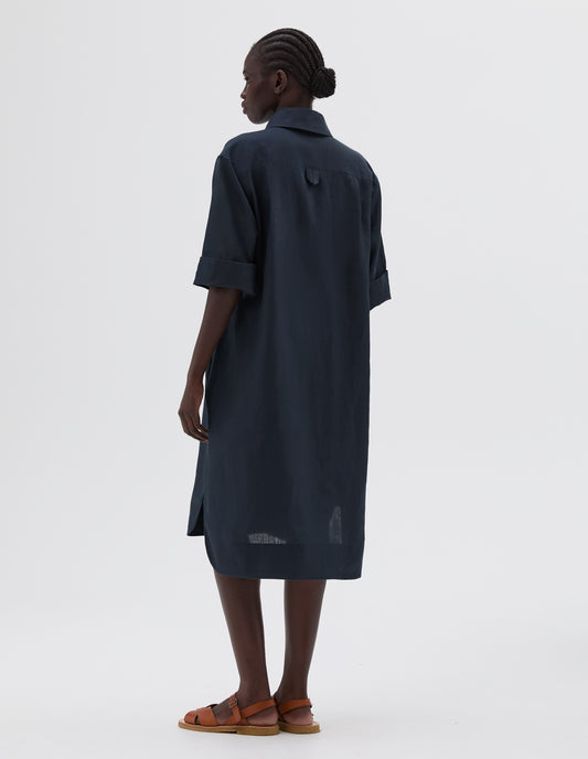 Full body image, back view of model wearing dark blue below the knee shirt dress with short sleeves and hanger loop detail on back, styled with light brown leather sandals.