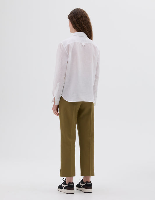 Full body image, back view of model wearing white linen shirt, with hanger loop on back yoke. Styled with cropped green trousers and brown and black trainers.