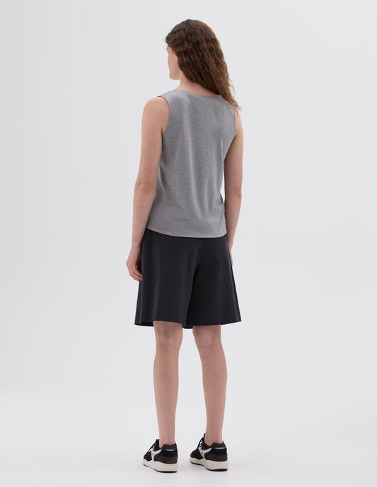 Full body image, back view of model wearing grey sleeveless vest. Styled with black shorts and black and brown trainers.