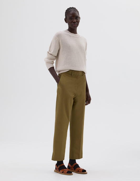 Full body image, front view of model wearing beige relaxed chunky crew neck jumper, styled with green trousers with side pockets and black socks with light brown leather sandals.