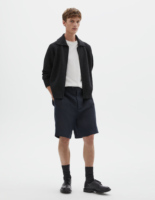 Full body image, front view of model wearing dark grey wool cardigan, with raglan sleeve, zip fastening and contrast rib on collar, cuffs and hem. Styled over a white t-shirt, with dark navy blue shorts, black socks and black leather brogues.