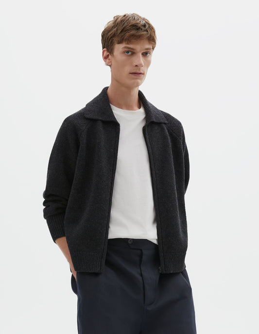 Cropped body image, front view of model wearing dark grey wool cardigan, with raglan sleeve, zip fastening and contrast rib on collar, cuffs and hem. Styled over a white t-shirt, with dark navy blue shorts.