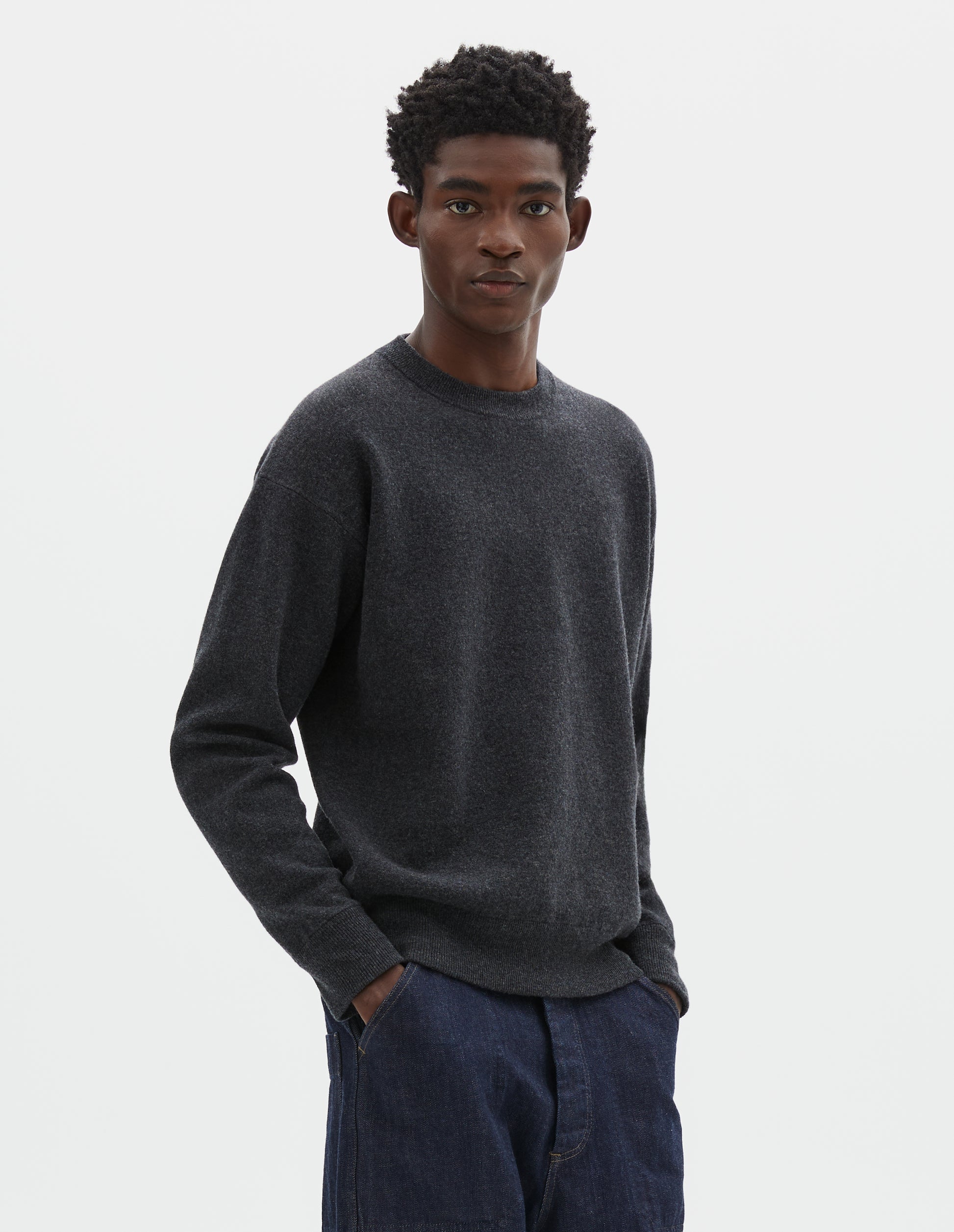 Cropped body image, front view of model wearing relaxed  dark grey knitted sweatshirt with rib collar, cuffs and hem. Styled with dark blue jeans.