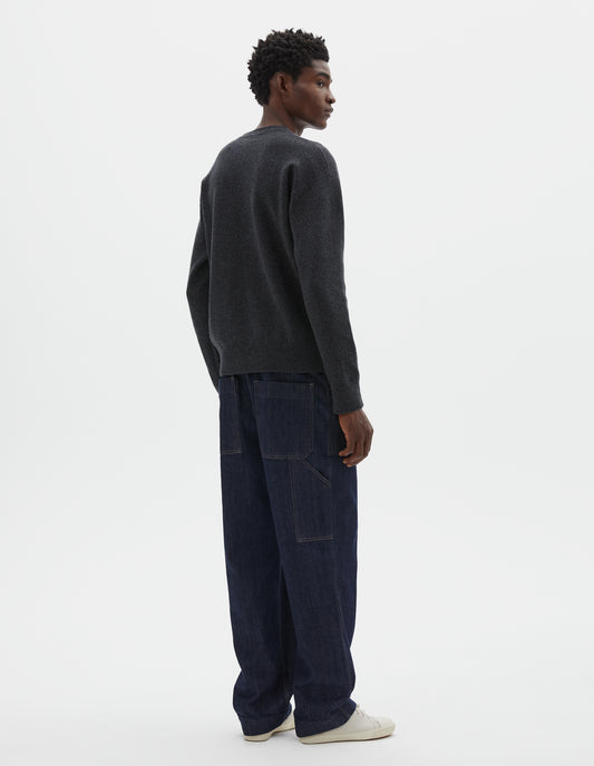 Full body image, back view of model wearing relaxed  dark grey knitted sweatshirt with rib collar, cuffs and hem. Styled with dark blue jeans and beige trainers.